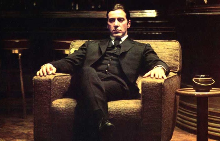 Al Pacino in character in the movie The Godfather, sitting in an upholstered chair staring outward, dispassionate and disconnected