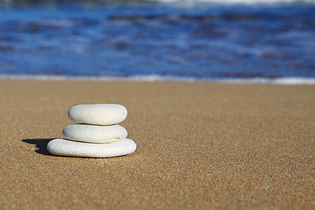 Three white beach pebbles balanced by graduated size on a brown sandy beach with a blue ocean in the background